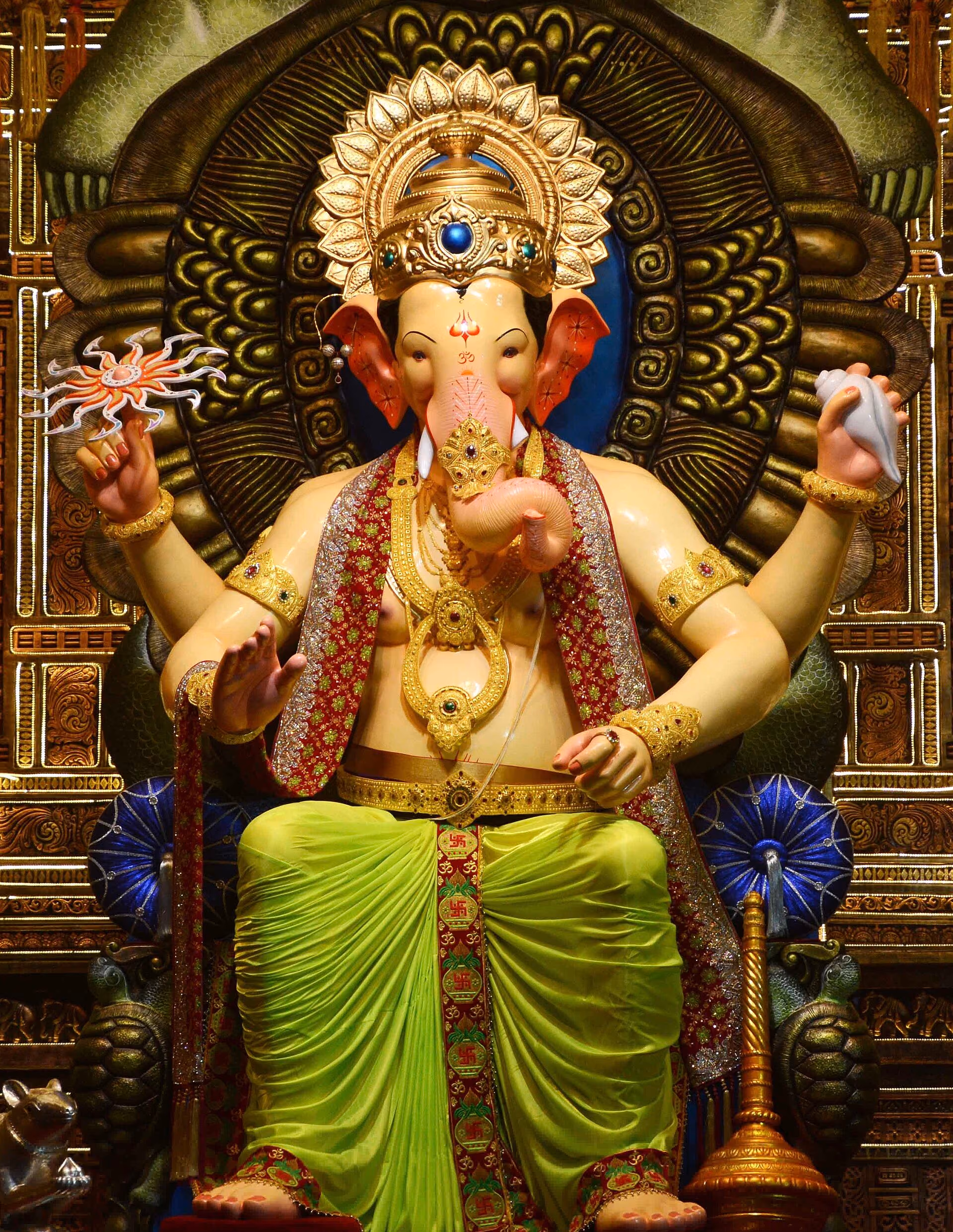 The Lalbaugcha Raja murti, crowned and richly ornamented, seated before a carved backdrop.